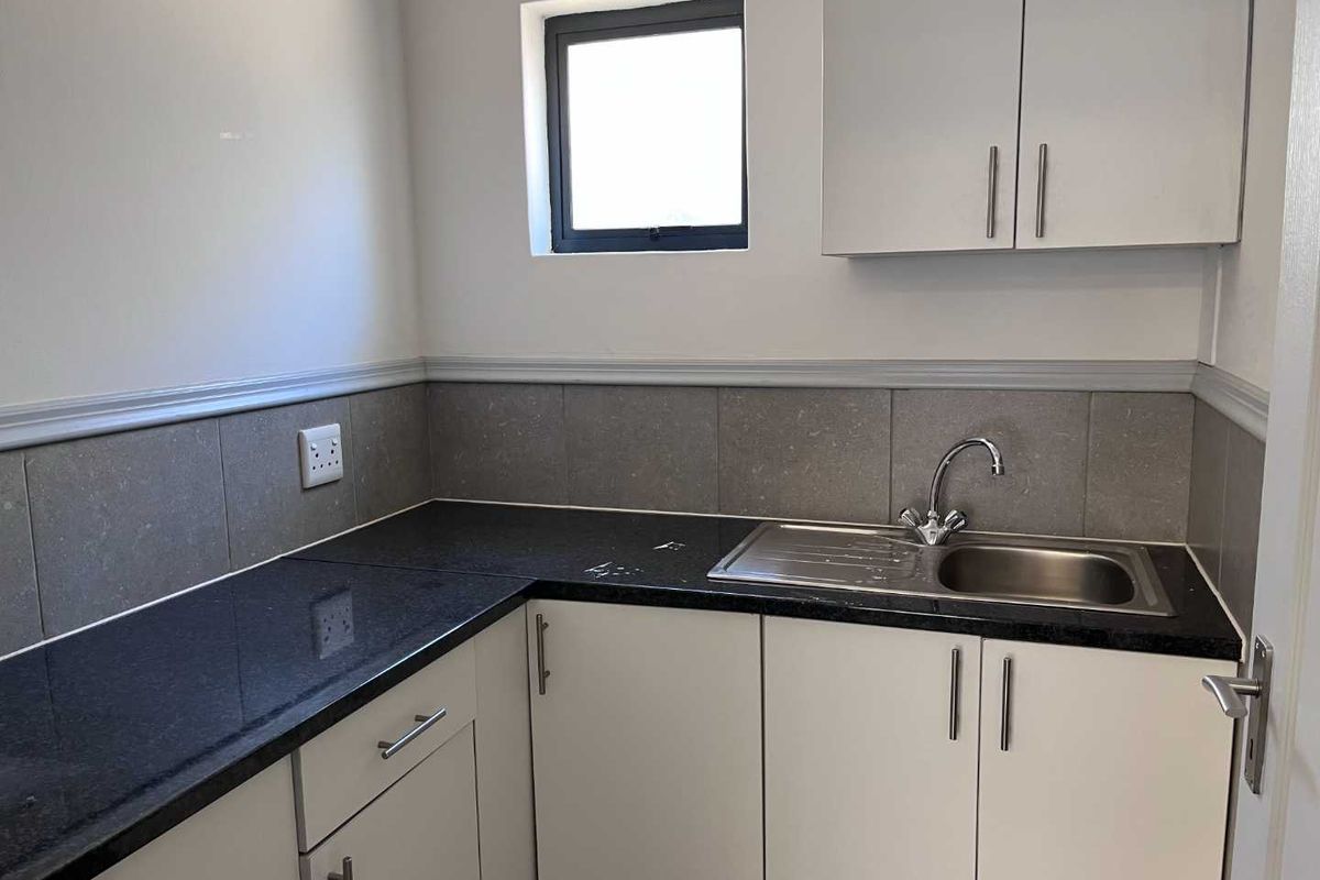 A compact kitchen area featuring modern white cabinetry, dark granite countertops, a stainless steel sink, and tiled splashbacks.