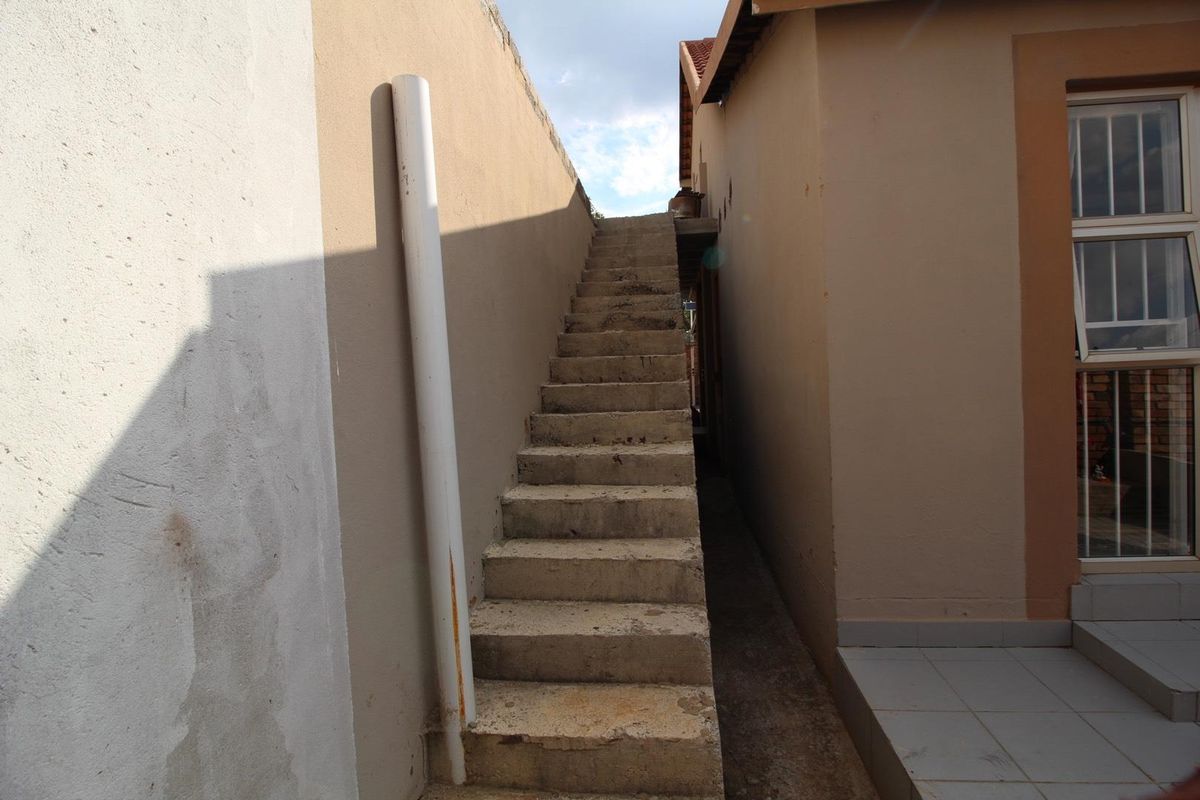 Exterior view of a narrow side passage featuring concrete stairs leading to an upper level, with adjacent building walls and a tiled entrance area.