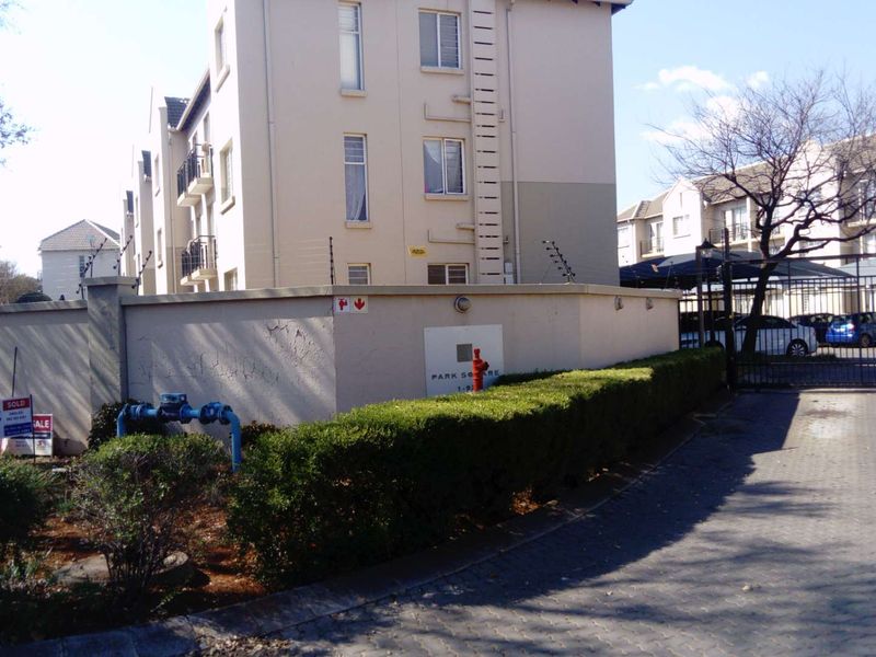 Exterior view of the apartment complex entrance featuring a perimeter wall, security gate, and paved driveway access.