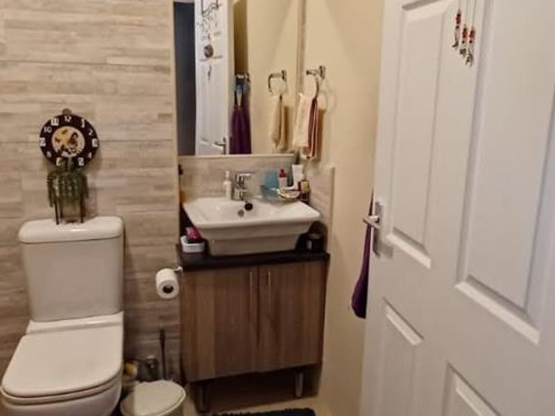 A compact bathroom featuring a modern vanity with basin, wall-mounted mirror, tiled feature wall, and neutral floor tiles.