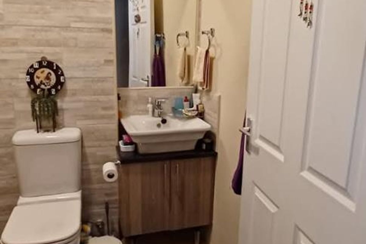 A compact bathroom featuring a modern vanity with basin, wall-mounted mirror, tiled feature wall, and neutral floor tiles.