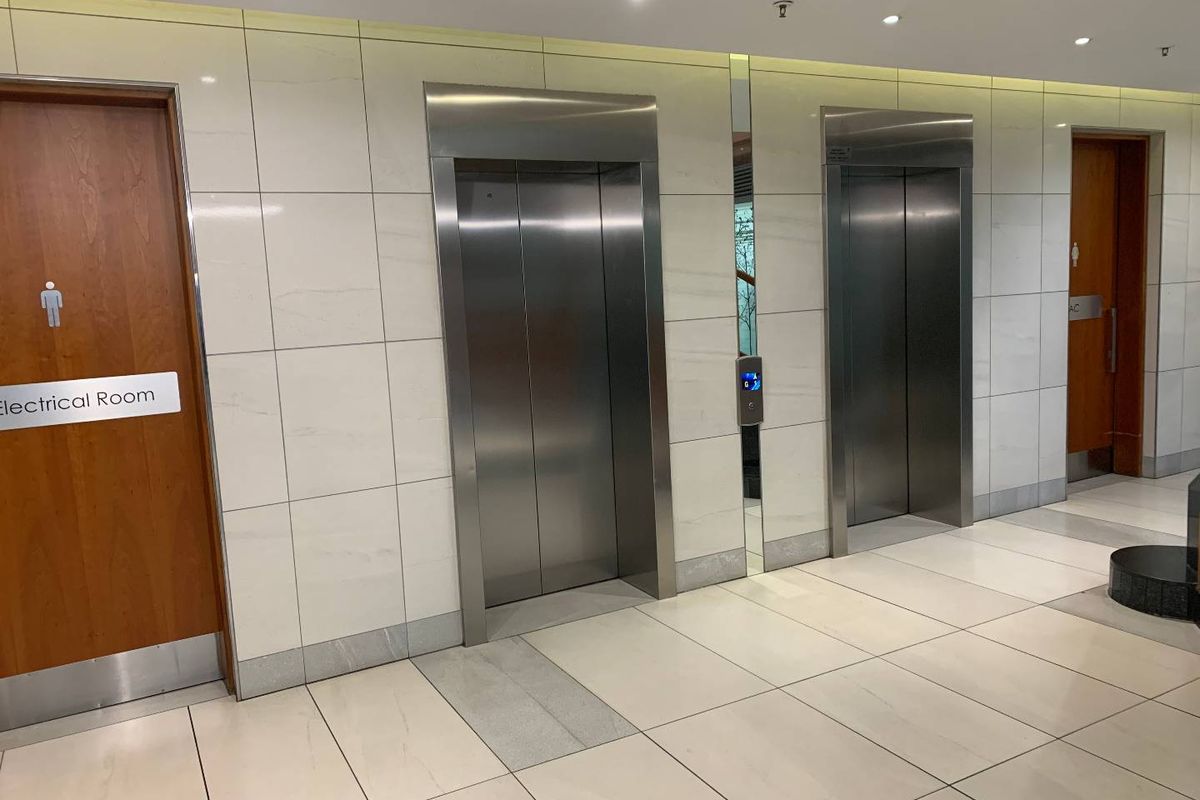 A modern office building hallway featuring stainless steel elevator banks, tiled wall finishes, and clean, well-maintained flooring.