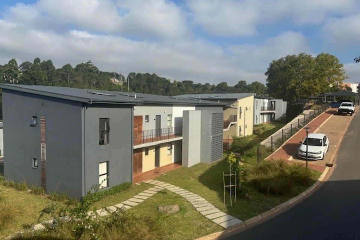 An elevated view of the apartment complex exterior, featuring modern grey and neutral facades, metal roofing, and landscaped grounds with paved walkways.
