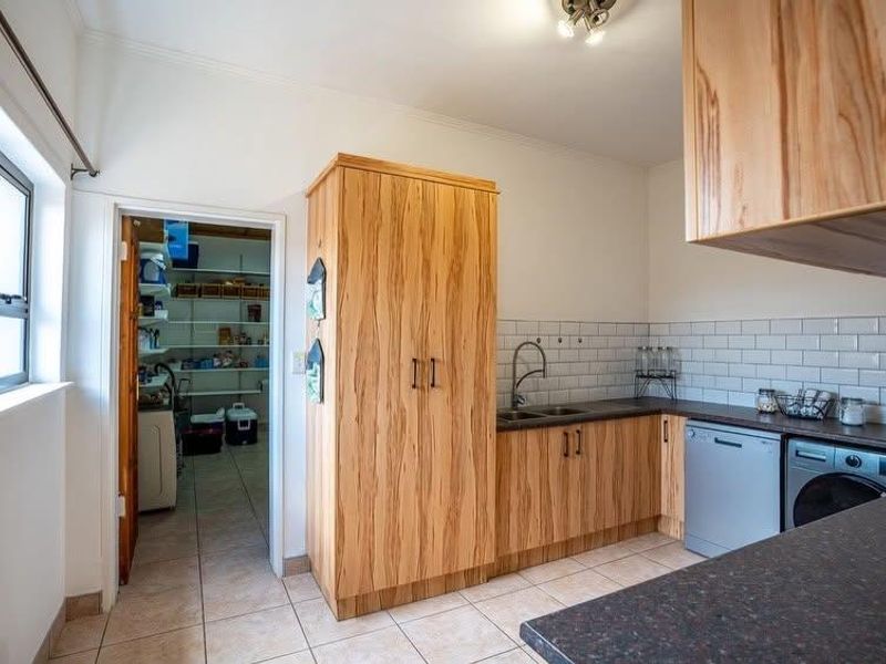 A functional scullery featuring wood-grain cabinetry, subway tile backsplash, double basin sink, and integrated dishwasher, with an adjacent walk-in pantry.