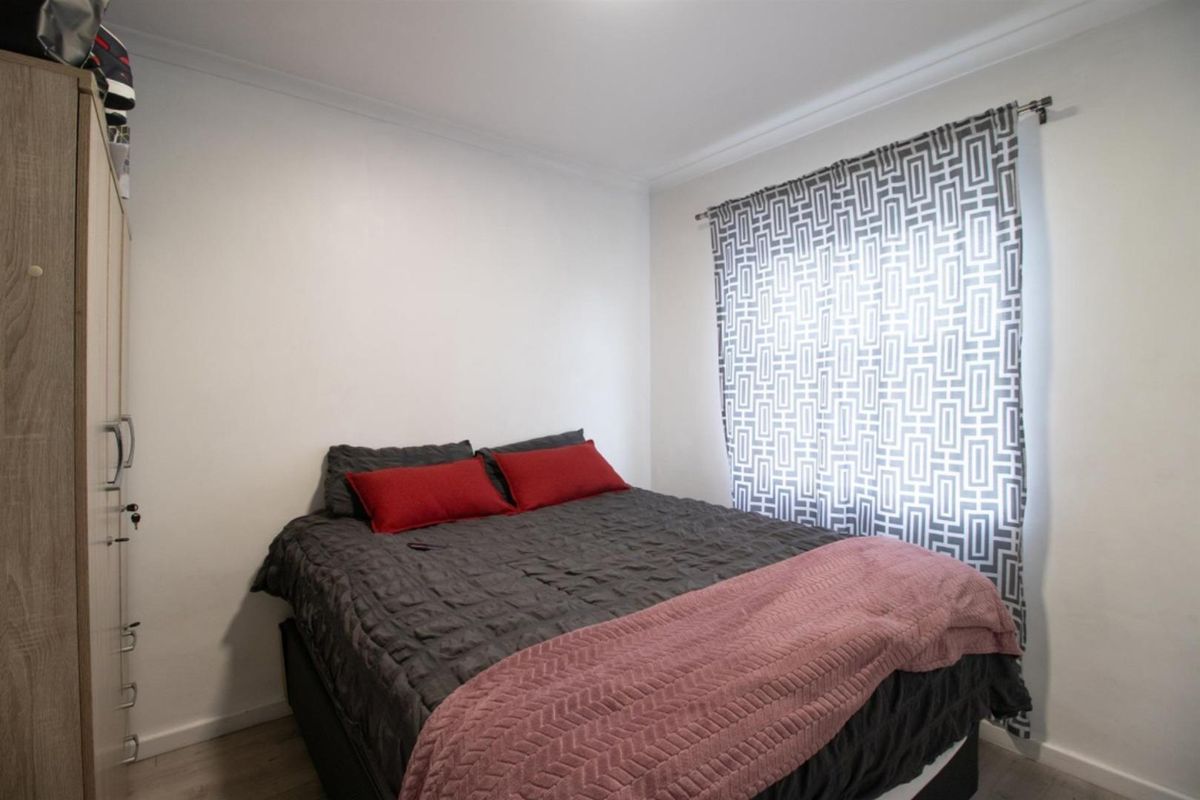 A compact bedroom featuring neutral walls, laminate flooring, and a window with patterned curtains.
