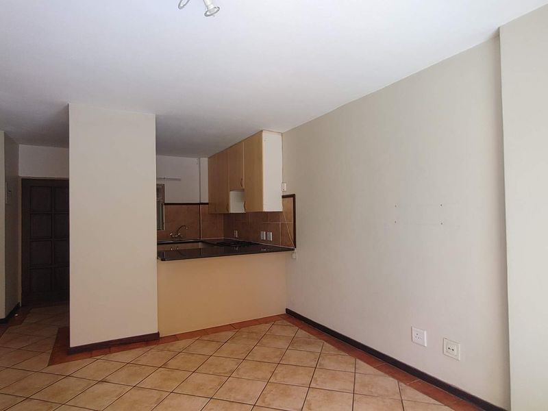 An open-plan living and kitchen area featuring tiled flooring, neutral walls, and functional kitchen cabinetry with granite countertops.