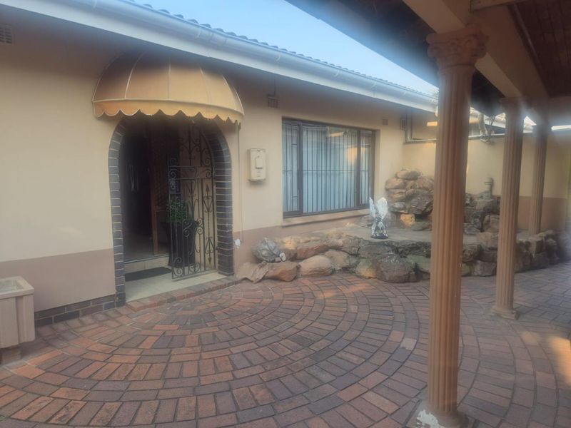Covered patio area featuring brick paving, decorative columns, and a rockery garden feature, providing a sheltered entrance to the home.