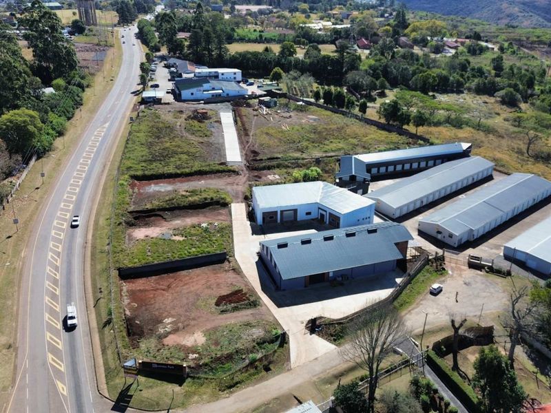 Aerial view of a commercial property featuring multiple warehouse structures, paved access, and significant undeveloped land adjacent to a main road.