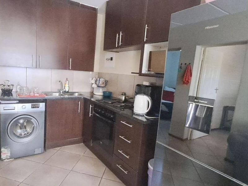 Compact kitchen featuring dark wood cabinetry, granite countertops, built-in oven, electric hob, and tiled flooring with an integrated laundry connection.