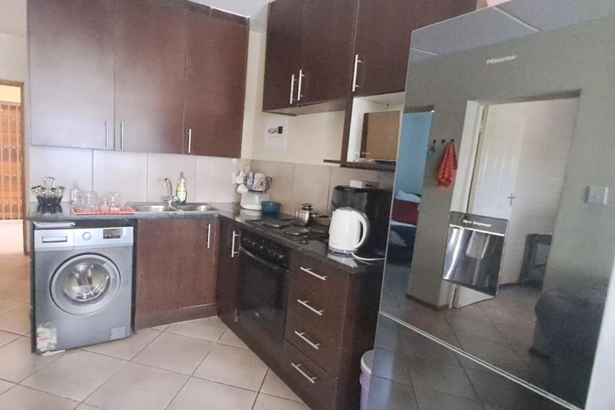 Compact kitchen featuring dark wood cabinetry, granite countertops, built-in oven, electric hob, and tiled flooring with an integrated laundry connection.