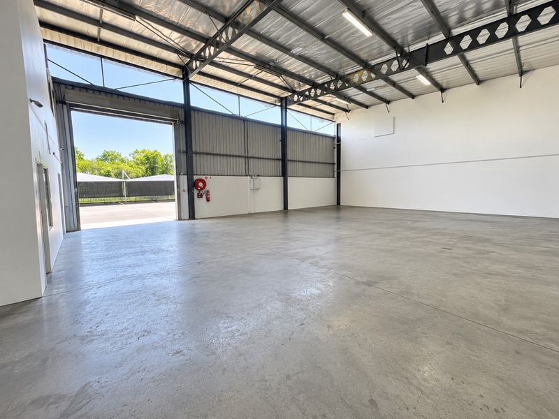 Spacious industrial warehouse unit featuring high ceilings, concrete flooring, and a large roller shutter door for easy access.