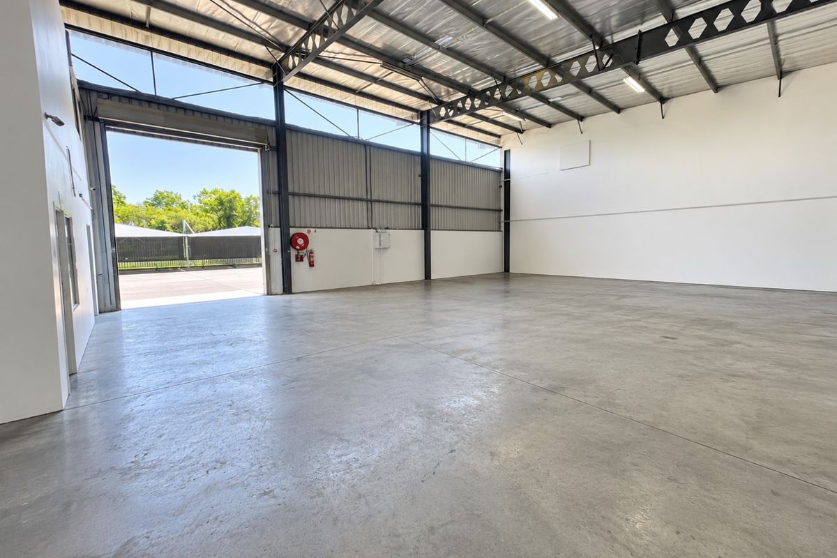 Spacious industrial warehouse unit featuring high ceilings, concrete flooring, and a large roller shutter door for easy access.