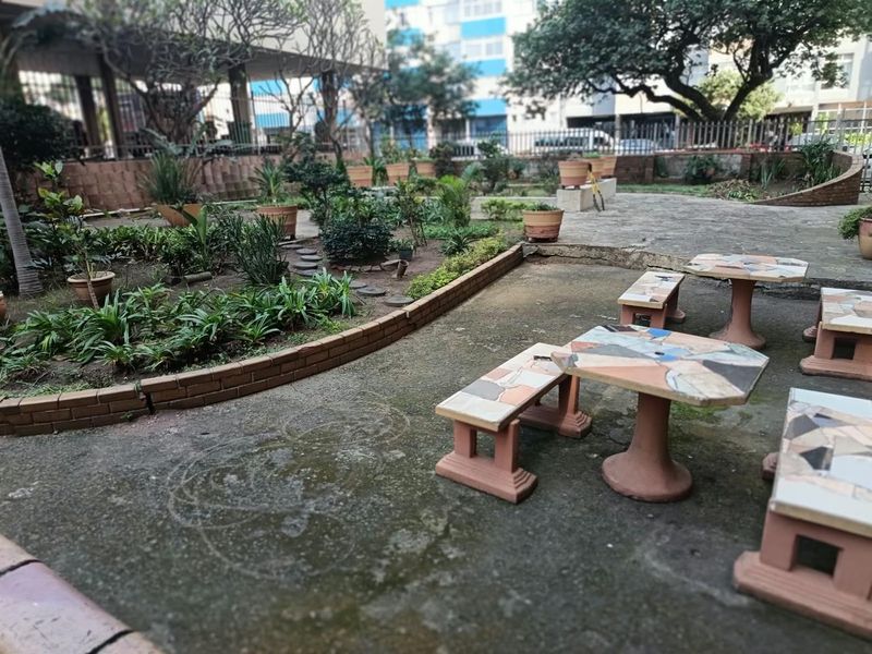 A communal outdoor garden area featuring paved pathways, brick retaining walls, and established garden beds in an apartment complex setting.