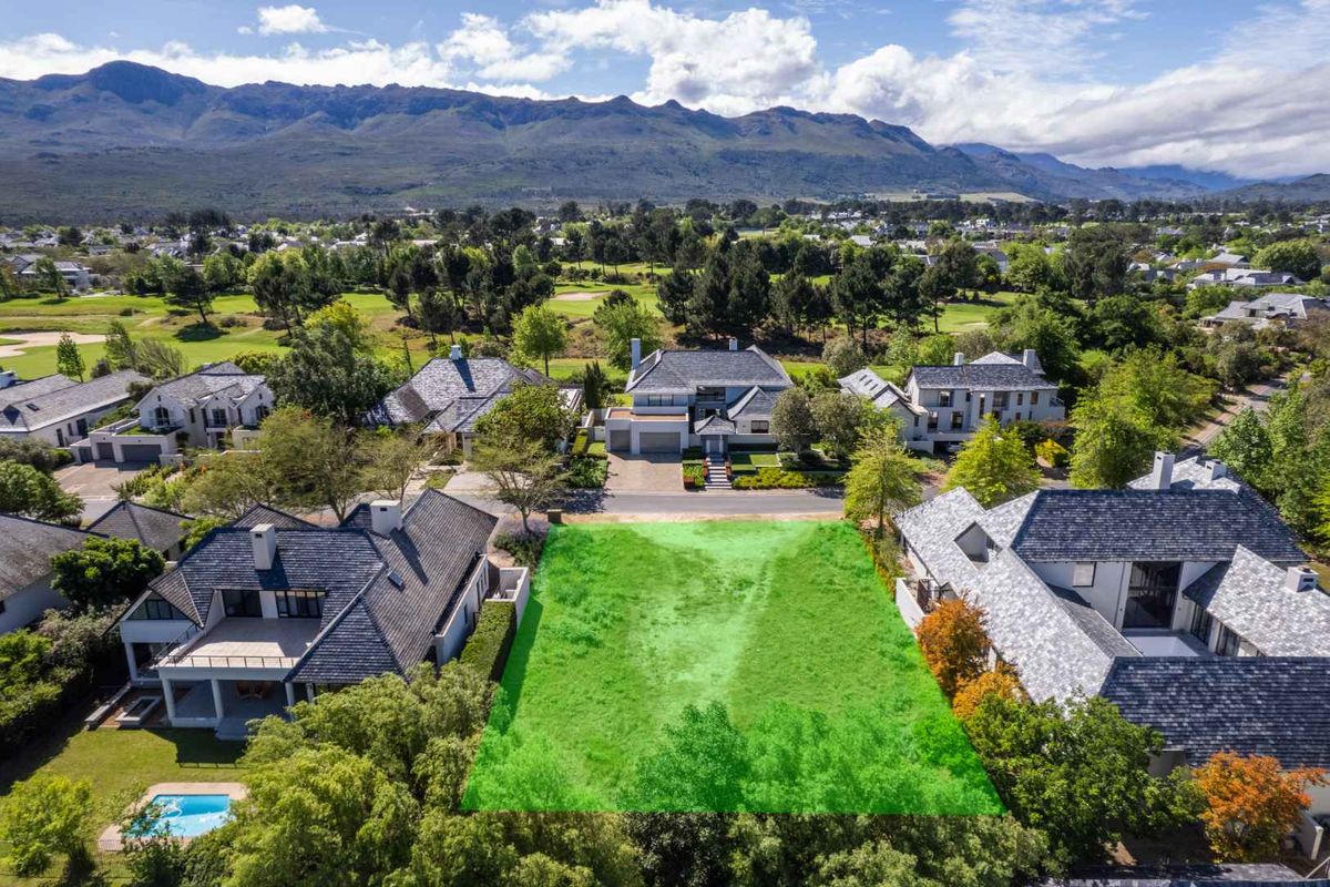 An aerial view of a vacant residential plot situated within an established estate, featuring surrounding luxury homes and scenic mountain views.