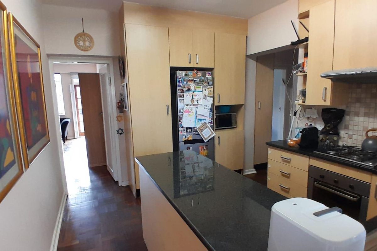A functional kitchen featuring light wood cabinetry, dark granite countertops, a gas hob, and a tiled backsplash, with direct access to the hallway.
