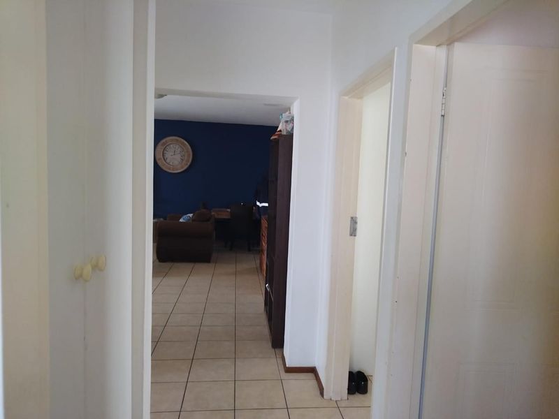 A functional hallway with tiled flooring leading into an open-plan living area, featuring neutral wall finishes and access to adjacent rooms.