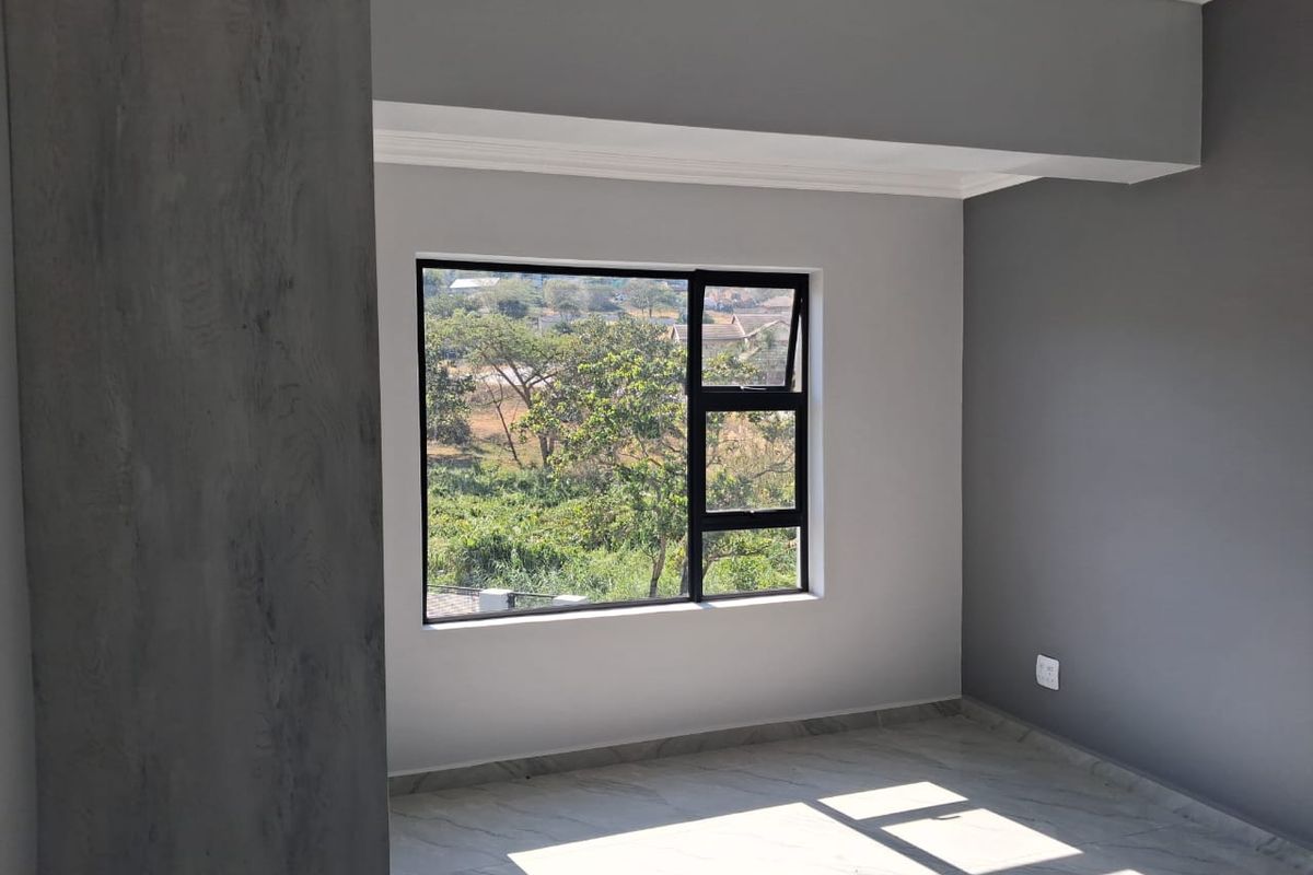 A bright, empty bedroom featuring modern grey painted walls, tiled flooring, and a large aluminium window with a scenic outdoor view.