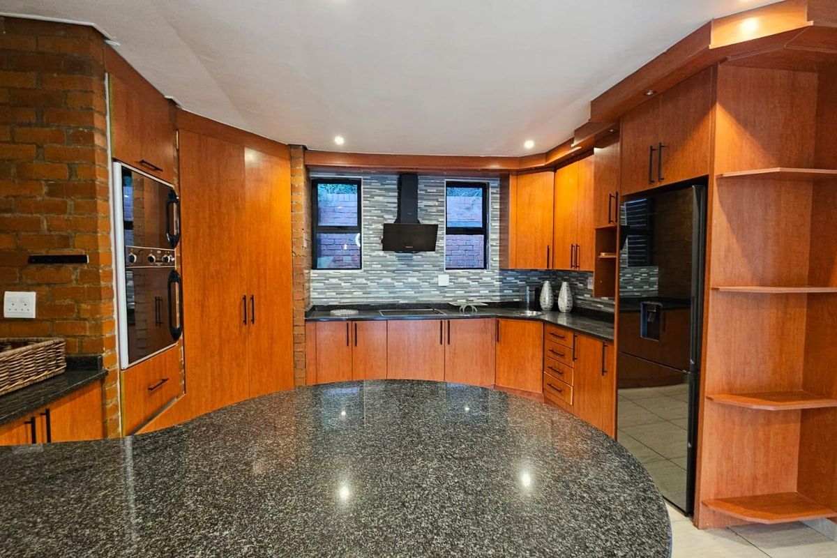 A well-appointed kitchen featuring warm wood cabinetry, granite countertops, a central island, built-in oven, and a modern tiled backsplash.
