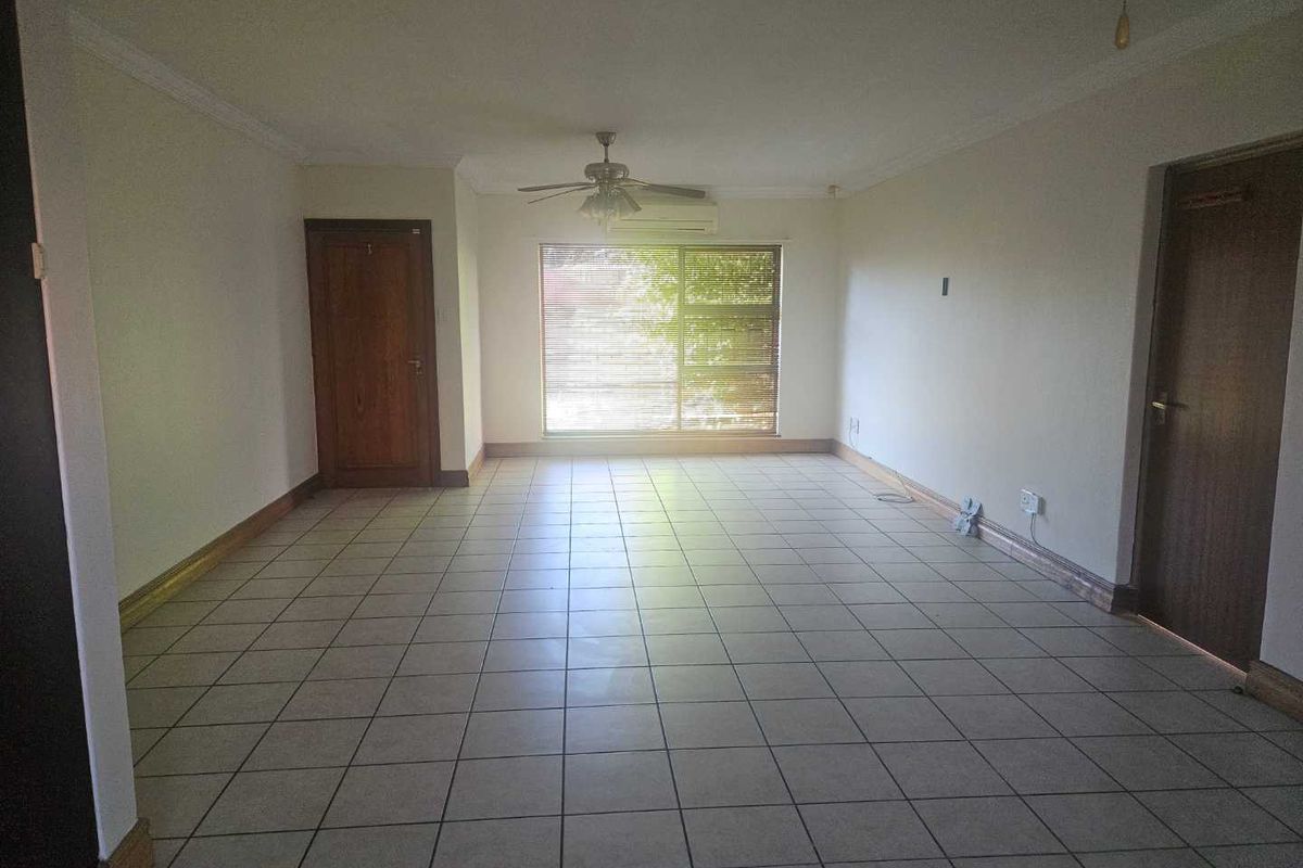 A spacious, empty living room featuring neutral tiled flooring, a ceiling fan, and a wall-mounted air conditioning unit.
