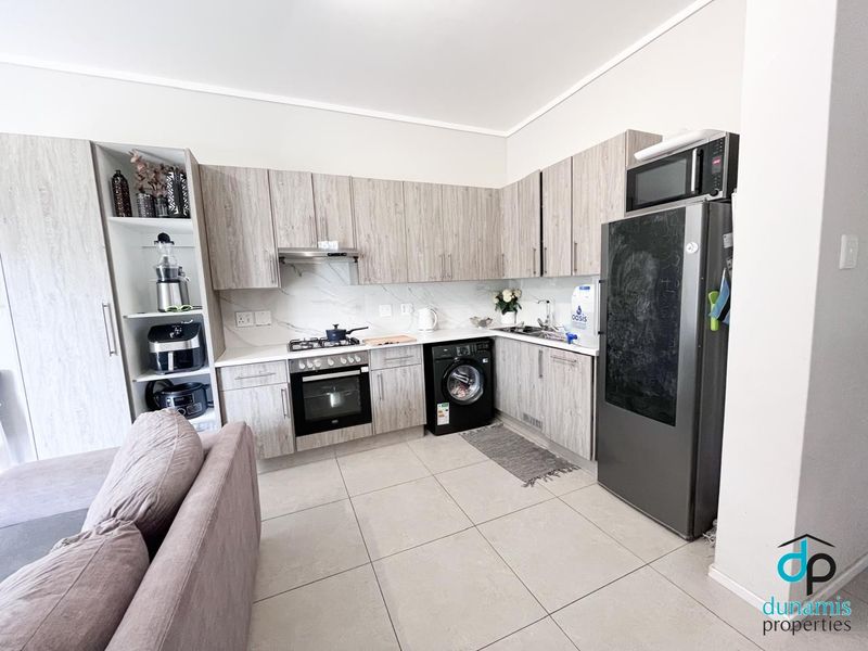 Modern open-plan kitchen featuring light wood-grain cabinetry, stone countertops, integrated appliances, and tiled flooring, seamlessly connecting to the living area.