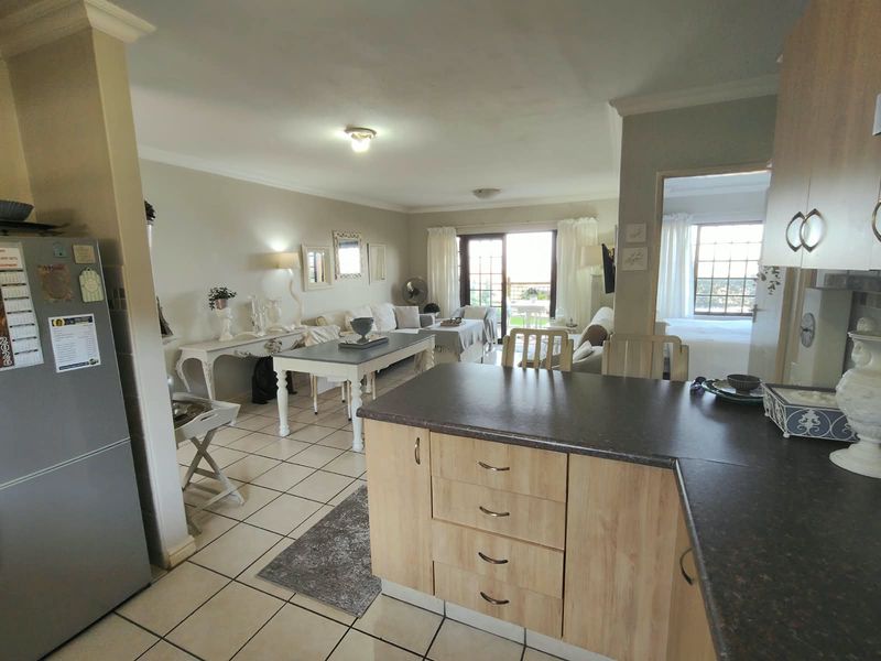 Open-plan living area featuring a kitchen with laminate cabinetry and tiled flooring, flowing into a lounge space with access to a patio.