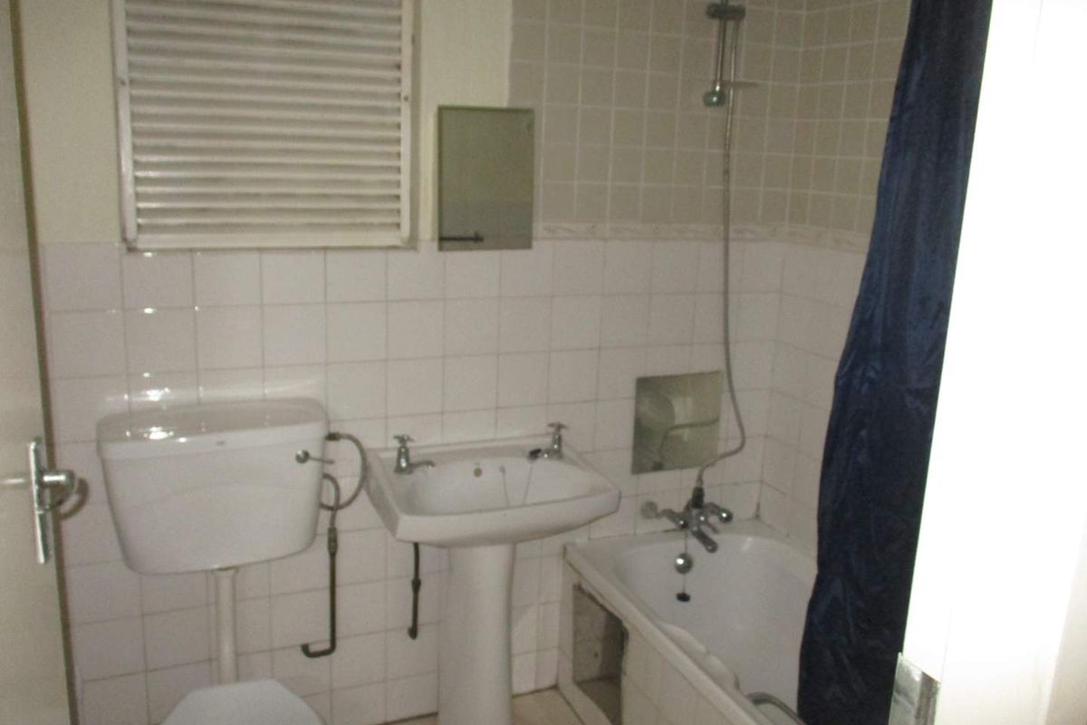 A functional bathroom featuring a pedestal basin, toilet, and a shower-over-bath combination with tiled walls.