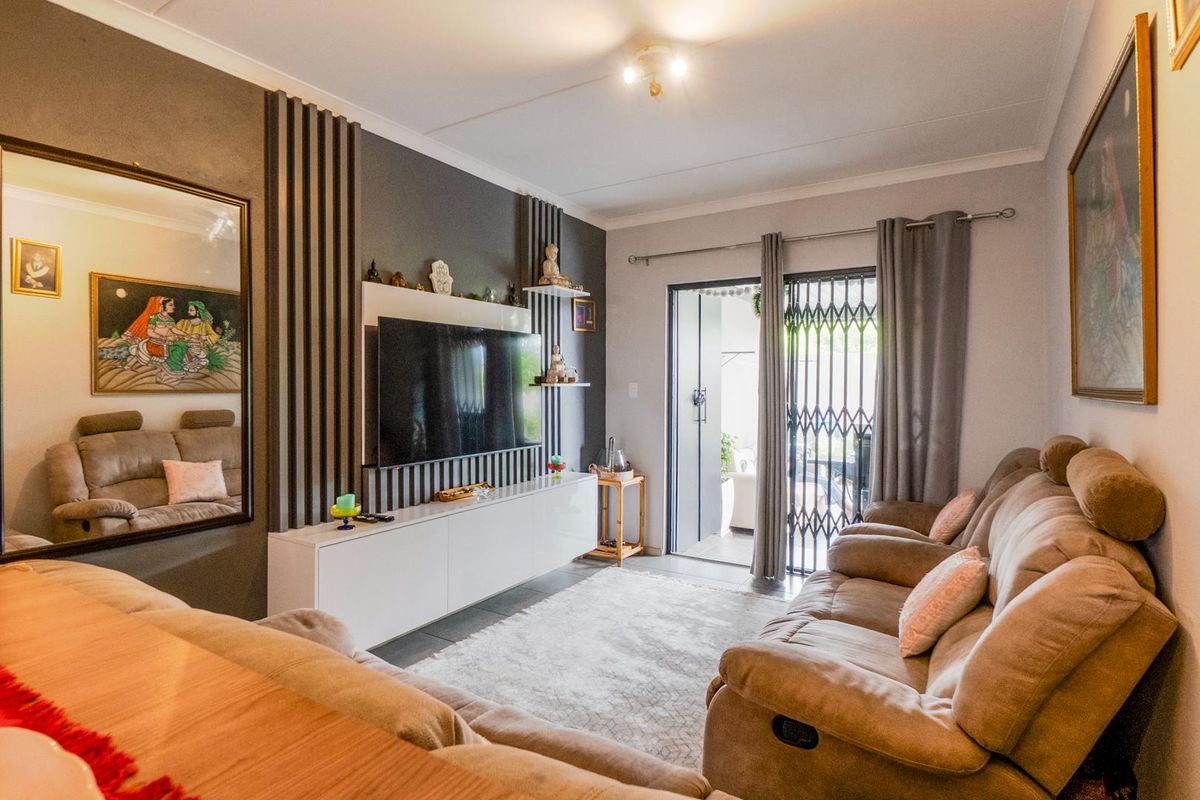 A well-maintained living room featuring a modern built-in media unit with vertical slat detailing and direct access to an outdoor patio area.