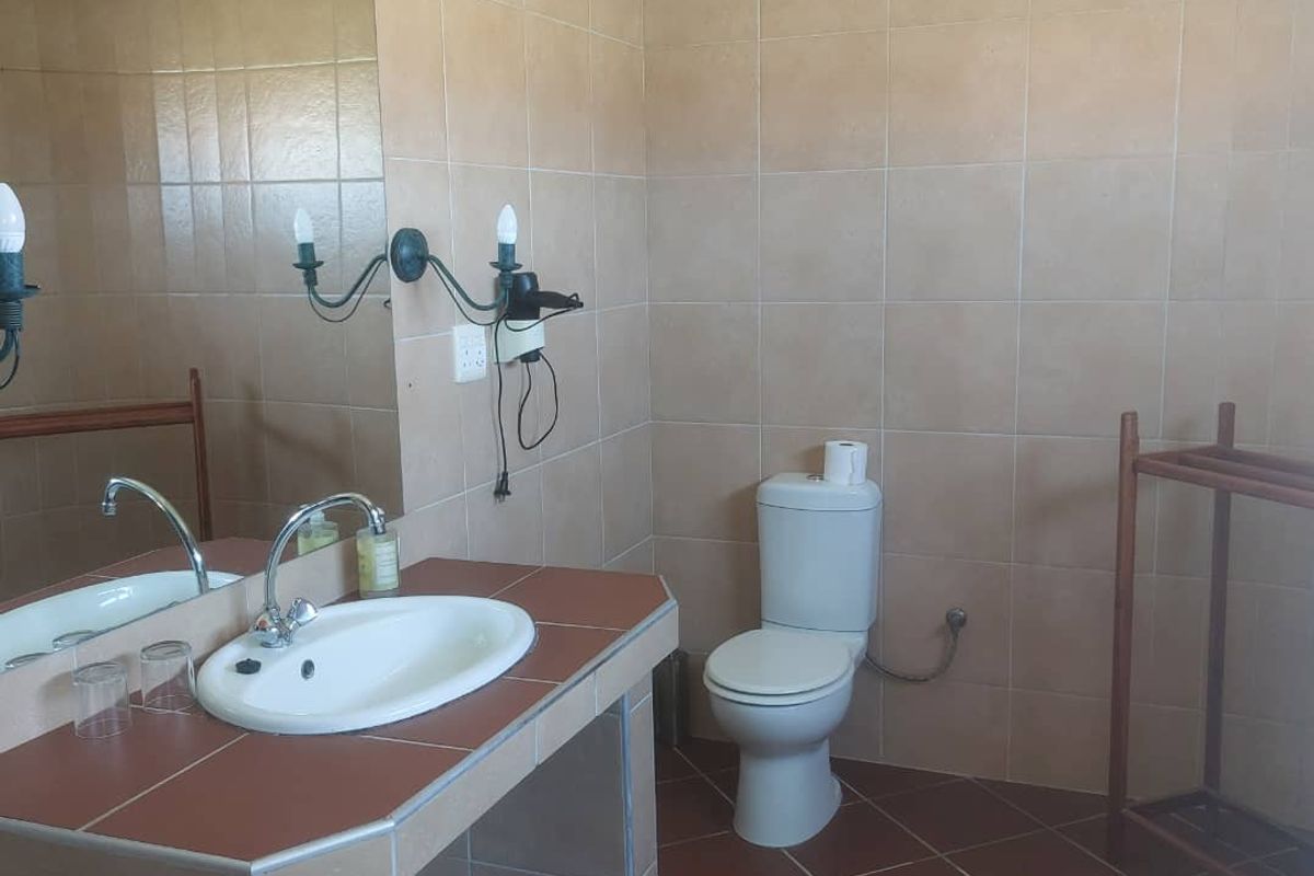A functional bathroom featuring a built-in vanity with a ceramic basin, wall-mounted mirror, and a standard toilet, finished with neutral wall and floor tiles.