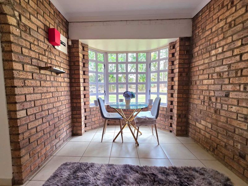A cozy living area featuring rustic exposed brick walls, tiled flooring, and a large bay window that provides ample natural light.