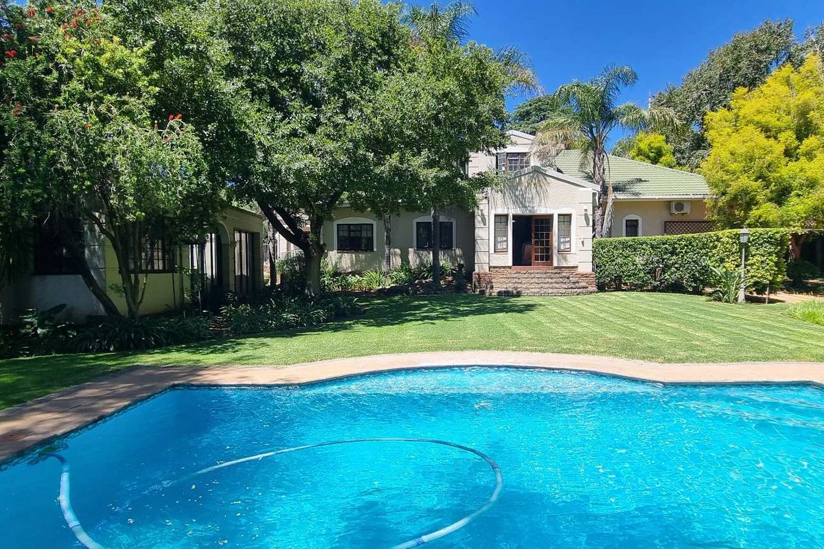 A well-maintained rear garden featuring a swimming pool, lush green lawn, mature trees, and a view of the house exterior.