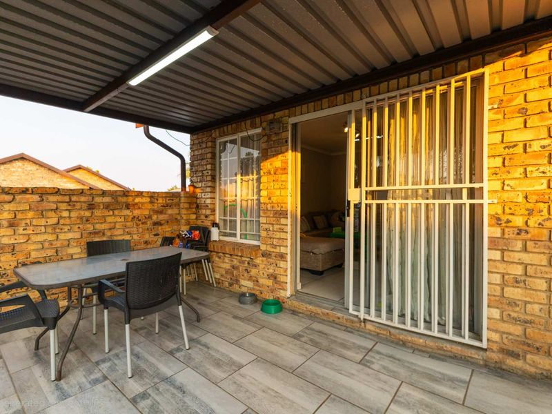 A covered patio area featuring brick walls, tiled flooring, and a security gate providing access to the interior living space.