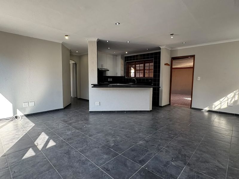 Spacious open-plan living area featuring dark tiled flooring, recessed lighting, and a functional kitchen with a breakfast bar.