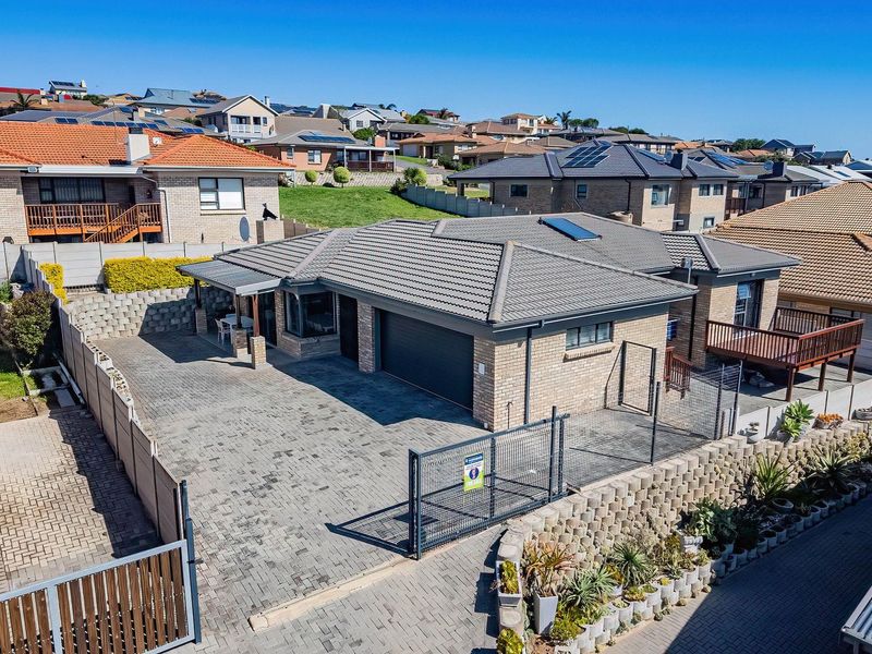 Aerial view of a brick-faced residential property featuring a paved driveway, double garage, tiled roof with solar panels, and a raised timber deck.