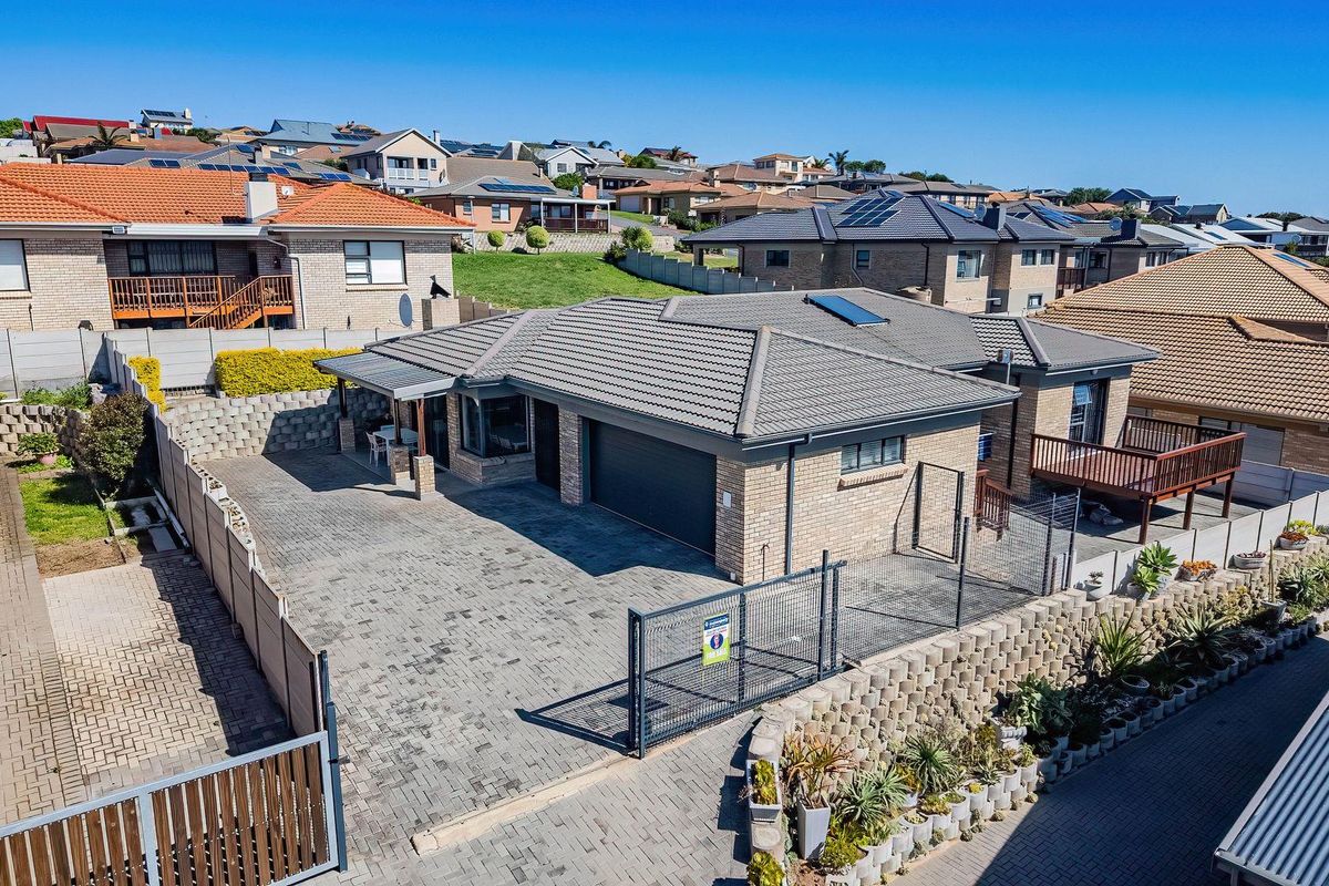 Aerial view of a brick-faced residential property featuring a paved driveway, double garage, tiled roof with solar panels, and a raised timber deck.