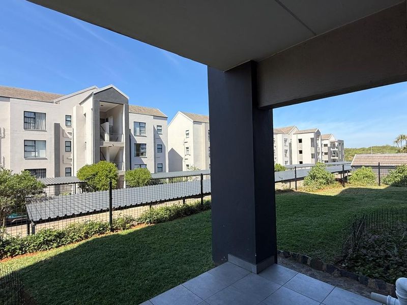 A covered ground-floor patio overlooking a shared garden area and adjacent apartment complex buildings.