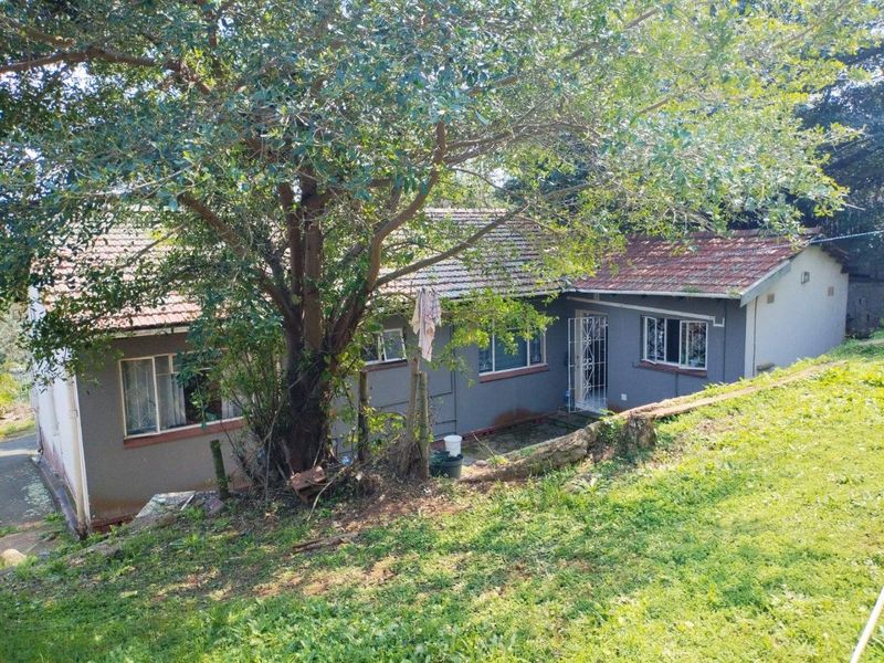 Rear view of a single-story house featuring a tiled roof, security gates, and a sloped garden area with a retaining wall.