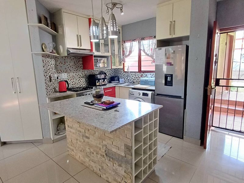 A functional kitchen featuring a stone-clad island with built-in wine storage, granite countertops, mosaic backsplash, and ample cabinetry, leading to an exterior security gate.
