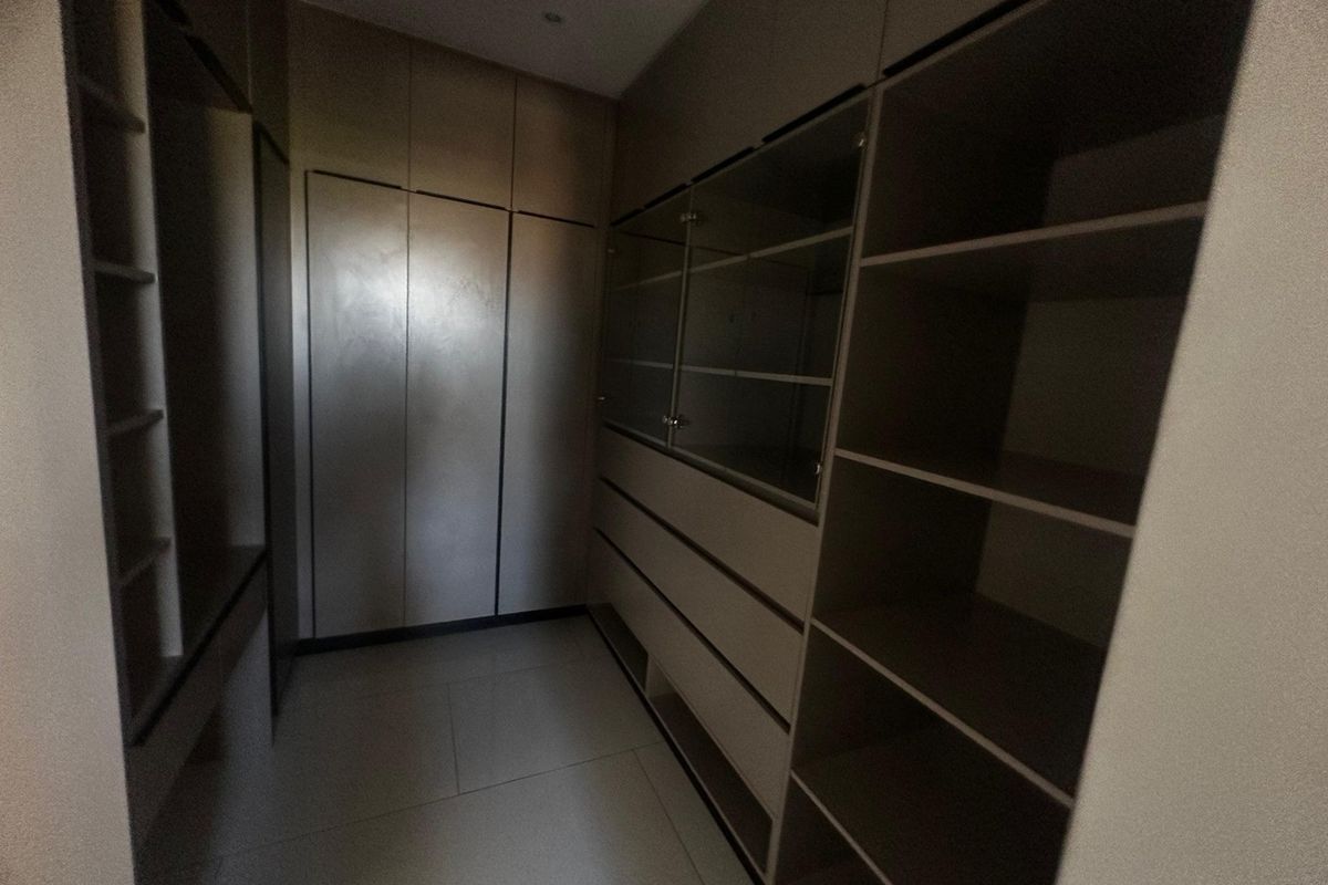 A modern walk-in closet or dressing room featuring extensive built-in cabinetry, glass-fronted storage, and clean tiled flooring.