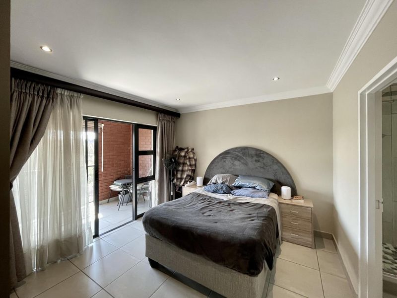 A well-maintained bedroom featuring tiled flooring, recessed downlighting, and a sliding glass door providing direct access to a private balcony.
