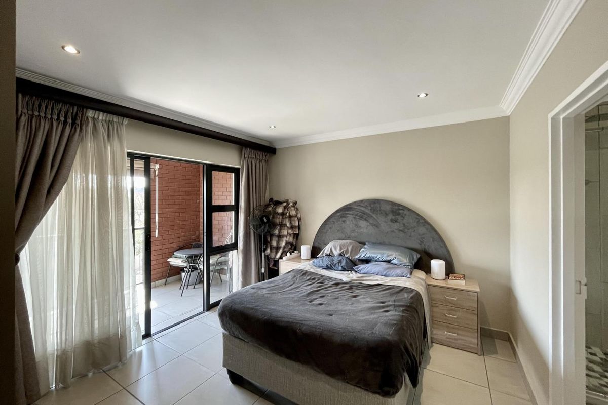A well-maintained bedroom featuring tiled flooring, recessed downlighting, and a sliding glass door providing direct access to a private balcony.