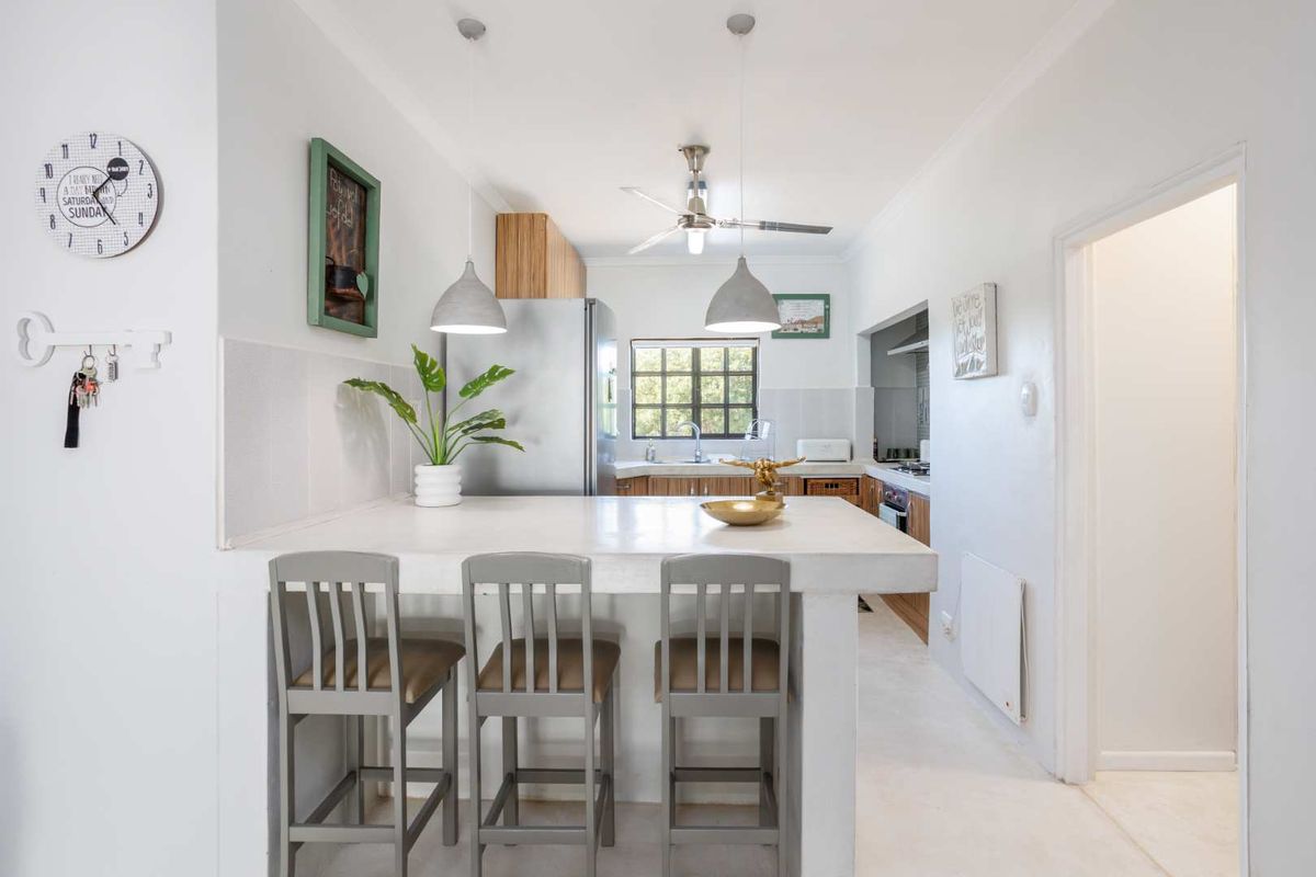A functional kitchen featuring a breakfast bar, wooden cabinetry, tiled splashbacks, and a ceiling fan, providing a practical layout for daily meal preparation.