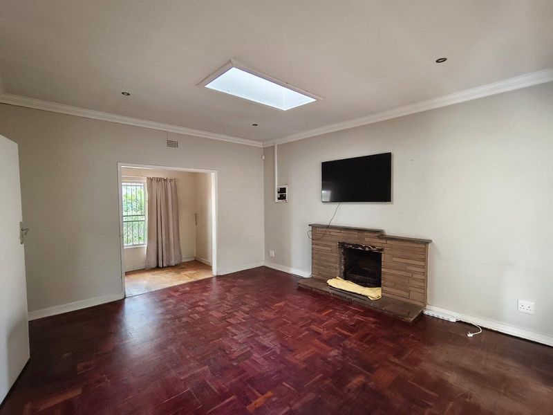 Spacious living room featuring original parquet flooring, a brick fireplace, and a central skylight, offering a bright and versatile living space.