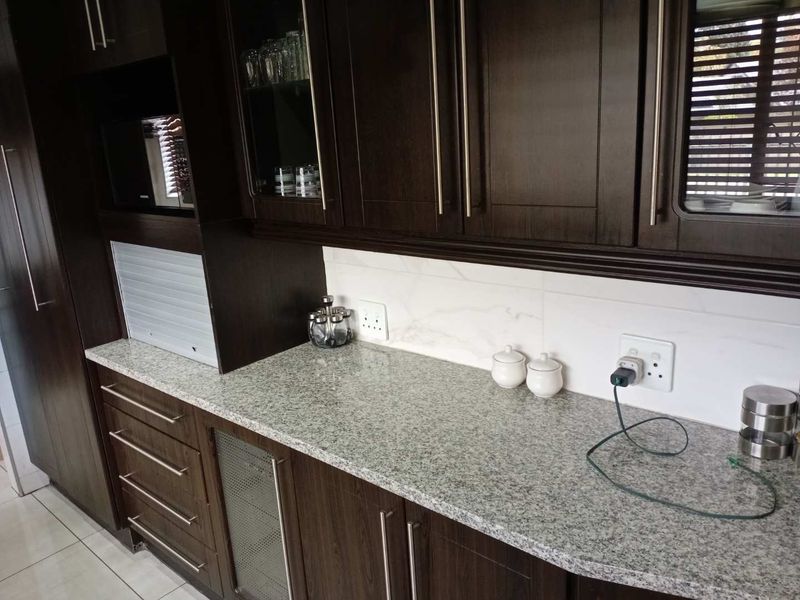 A well-maintained kitchen featuring dark wood cabinetry, granite countertops, a tiled backsplash, and a convenient built-in appliance garage.