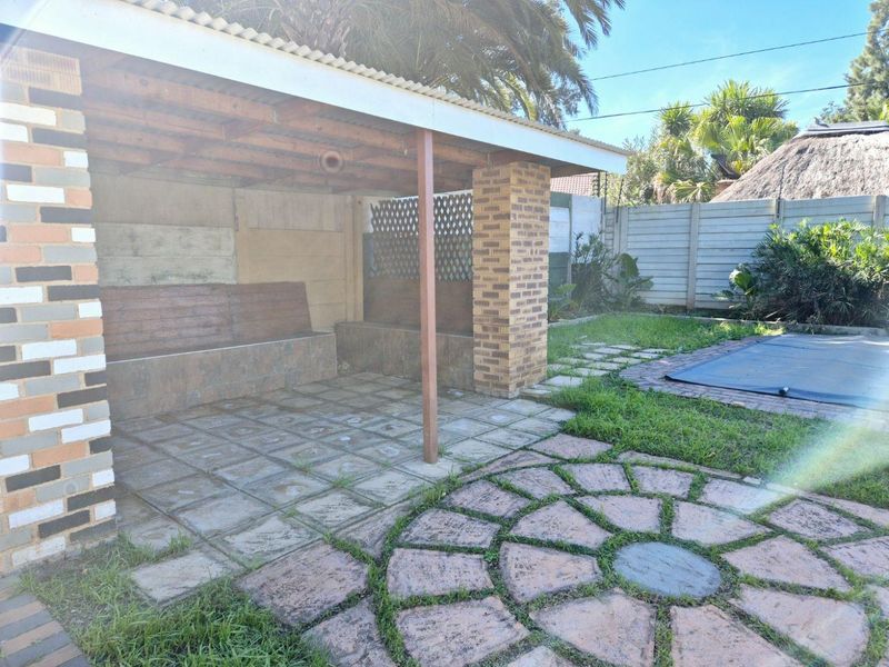 A covered outdoor patio area featuring brick pillars and a built-in bench, adjacent to a garden space with paved pathways.