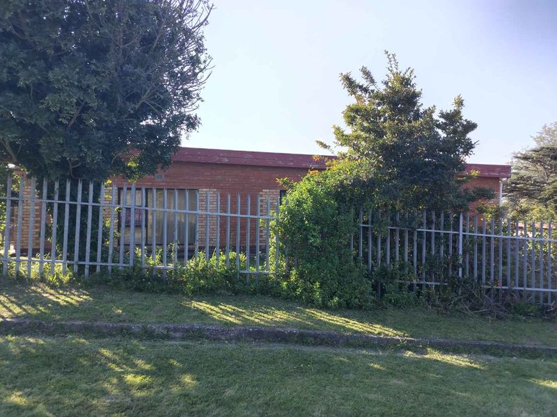 Front view of a single-story brick house featuring metal security fencing and mature garden landscaping.