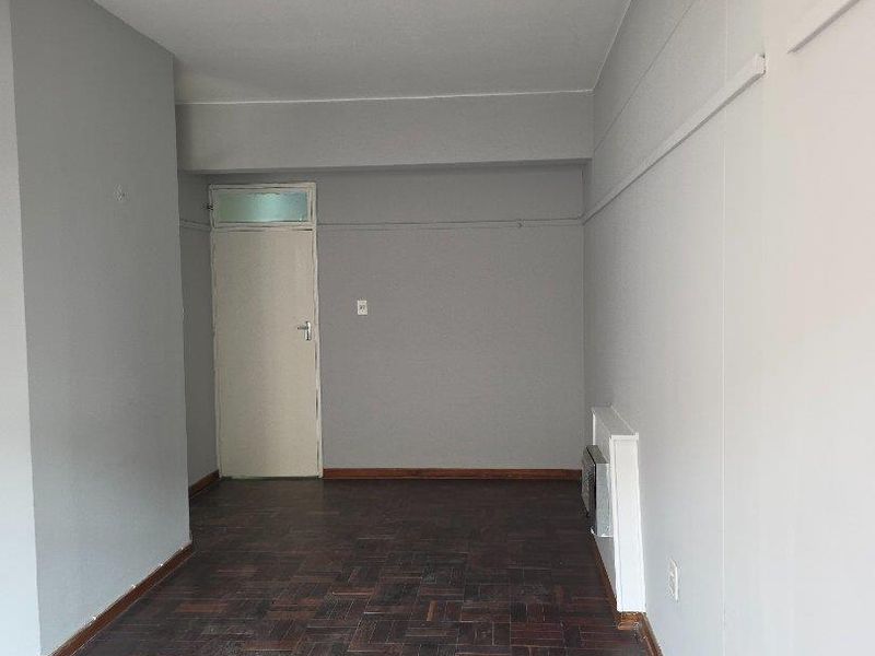 An empty living area featuring traditional parquet flooring and neutral wall tones, offering a blank canvas for interior design.