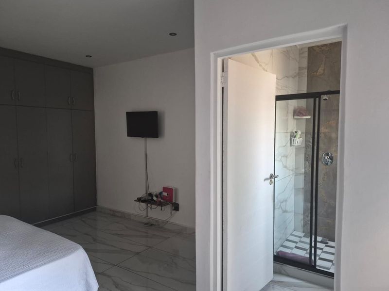 A modern bedroom featuring sleek tiled flooring, built-in cupboards, and an en-suite bathroom with a glass-enclosed shower.