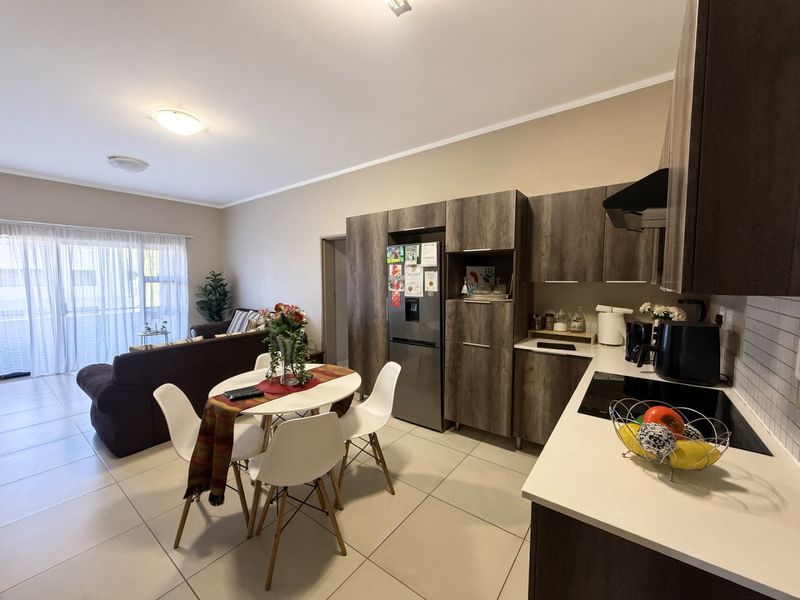 Modern open-plan living area featuring a contemporary kitchen with dark wood cabinetry, sleek countertops, and seamless flow to the adjacent living space and balcony.