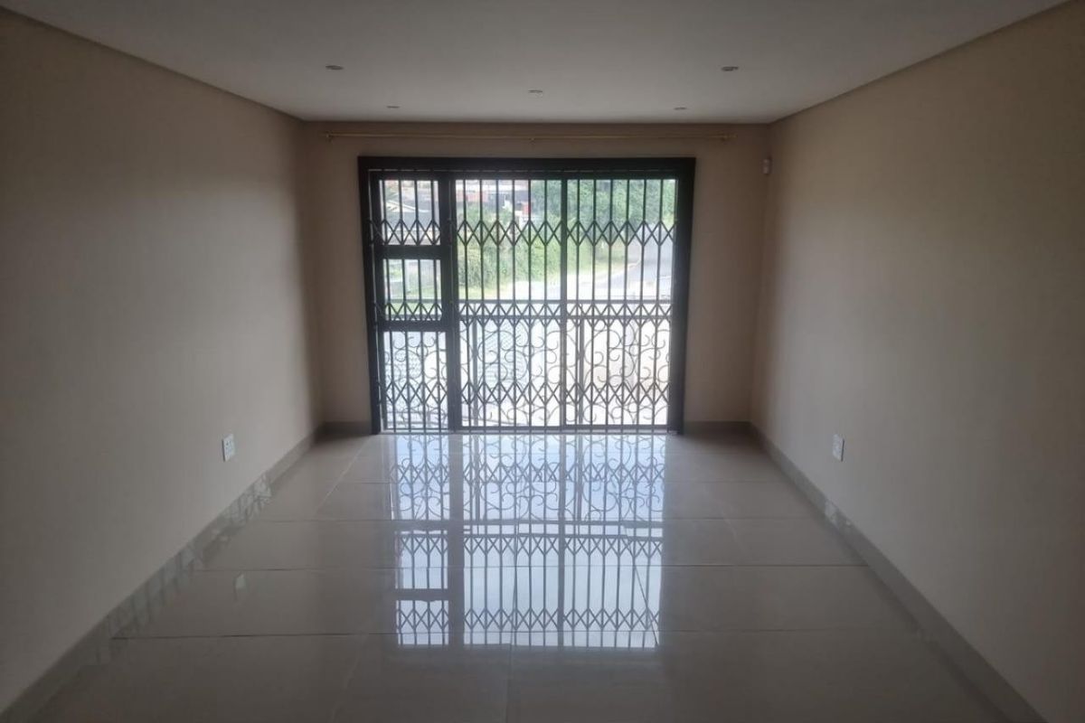 An empty, well-maintained living area featuring neutral tiled flooring, recessed downlights, and a secure sliding door with an integrated security gate.