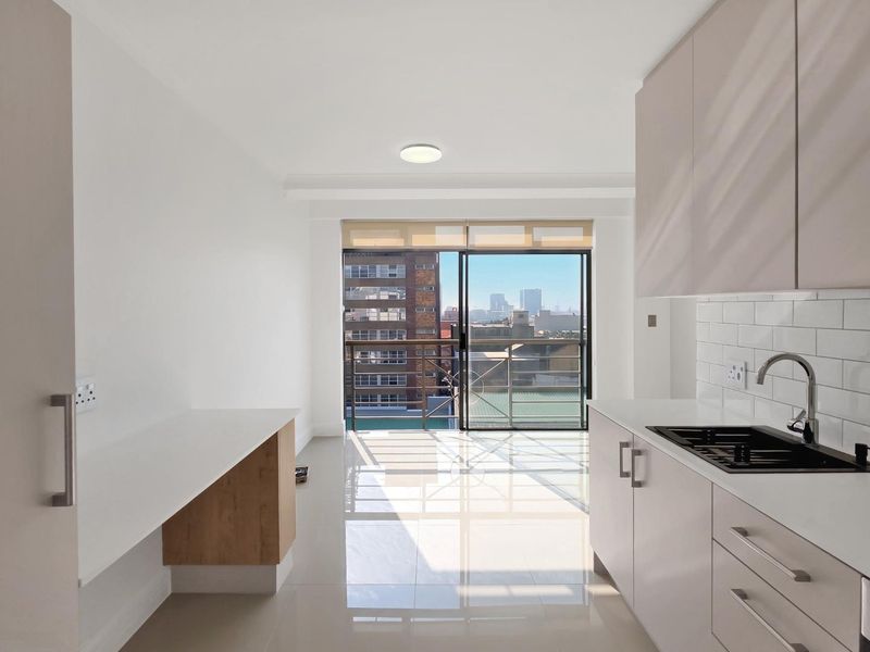 Modern open-plan kitchen and living area featuring sleek cabinetry, subway tile backsplash, and a sliding door leading to a balcony with city views.